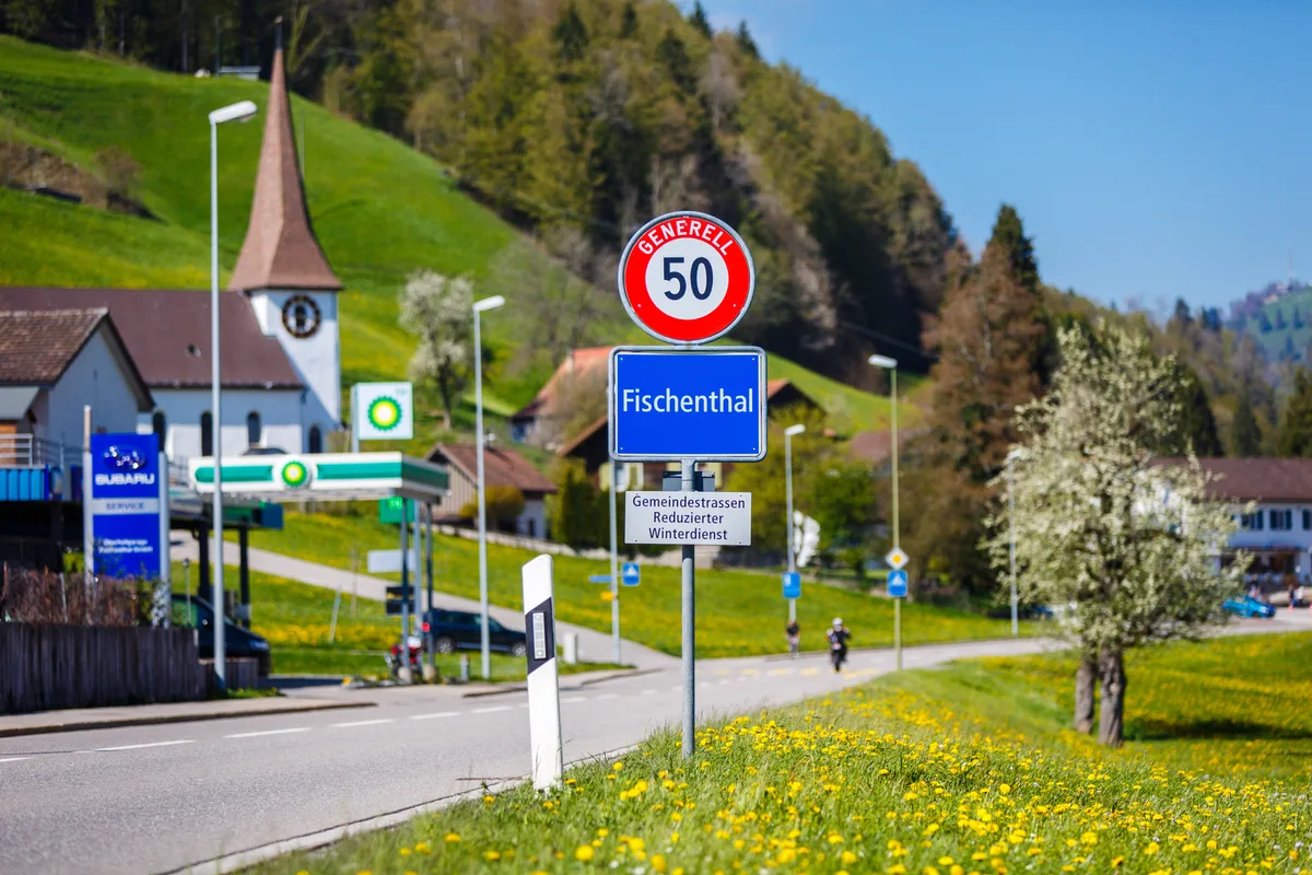 Ortsschild von Fischenthal und im Hintergrund die Kirche.